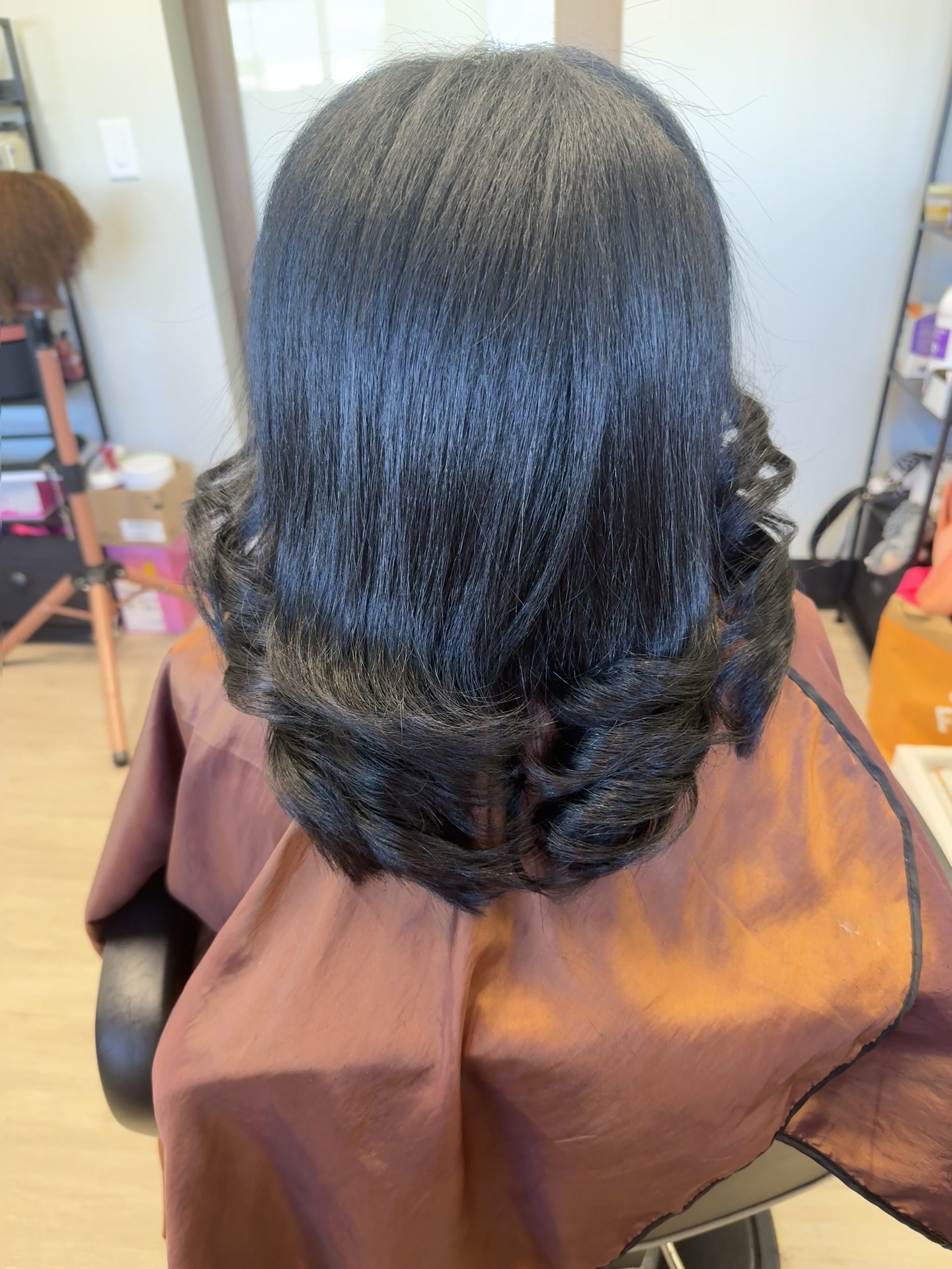 Back view of dark shoulder-length hair styled smooth at the crown with soft curled ends.