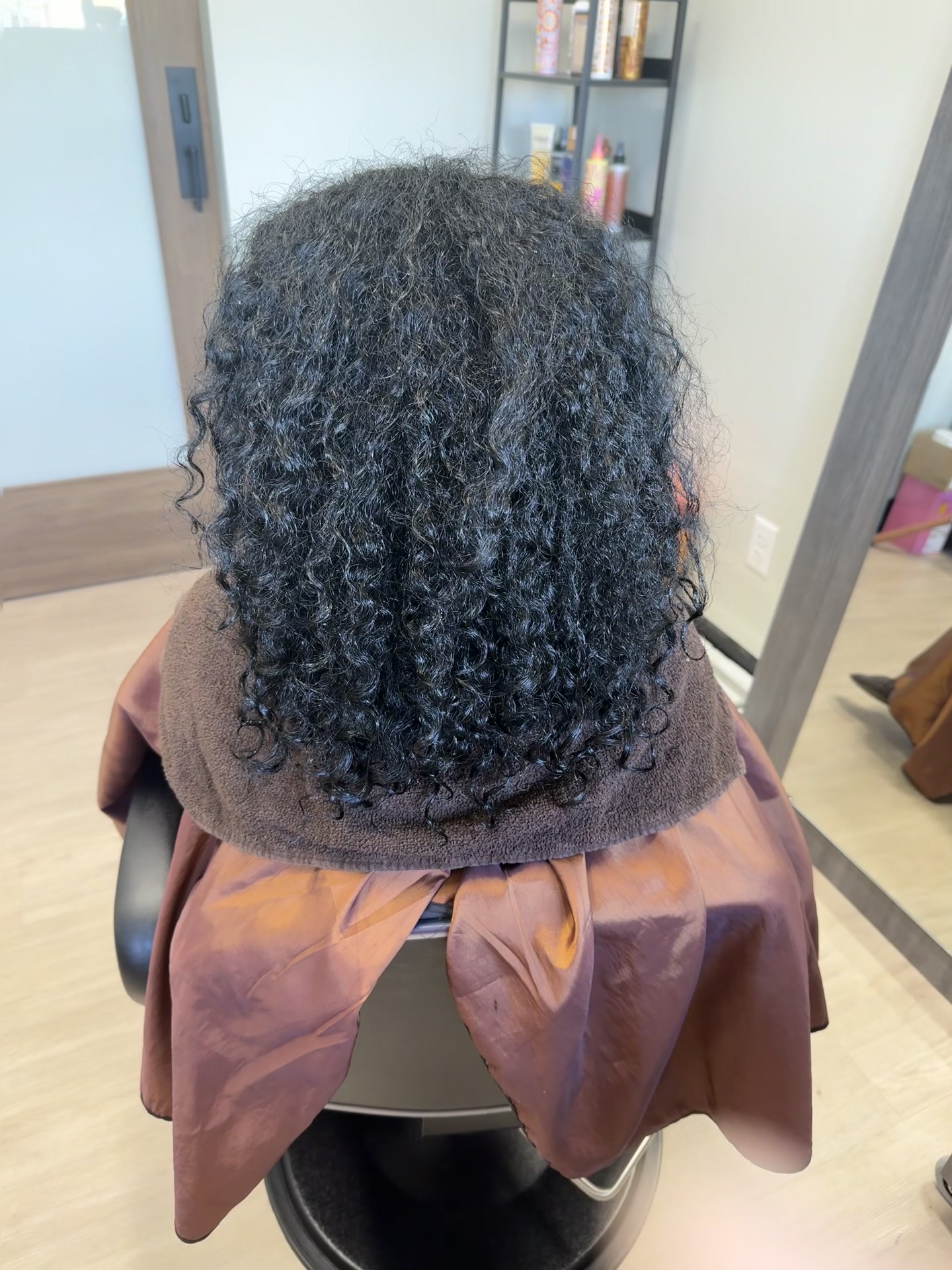 Back view of shoulder-length dark natural curls with defined coils, photographed in the salon.